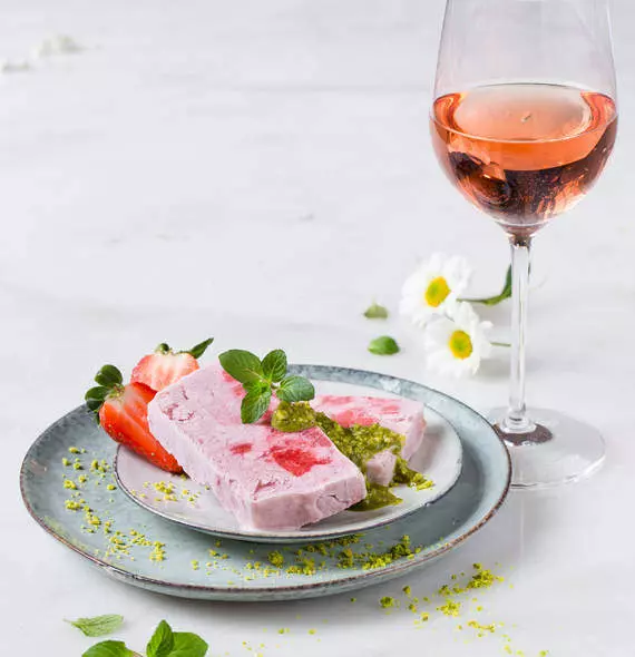 Un dessert à base de glace aux fraises, servi avec des fraises fraîches et de la sauce verte, accompagné d'un verre de vin rosé.